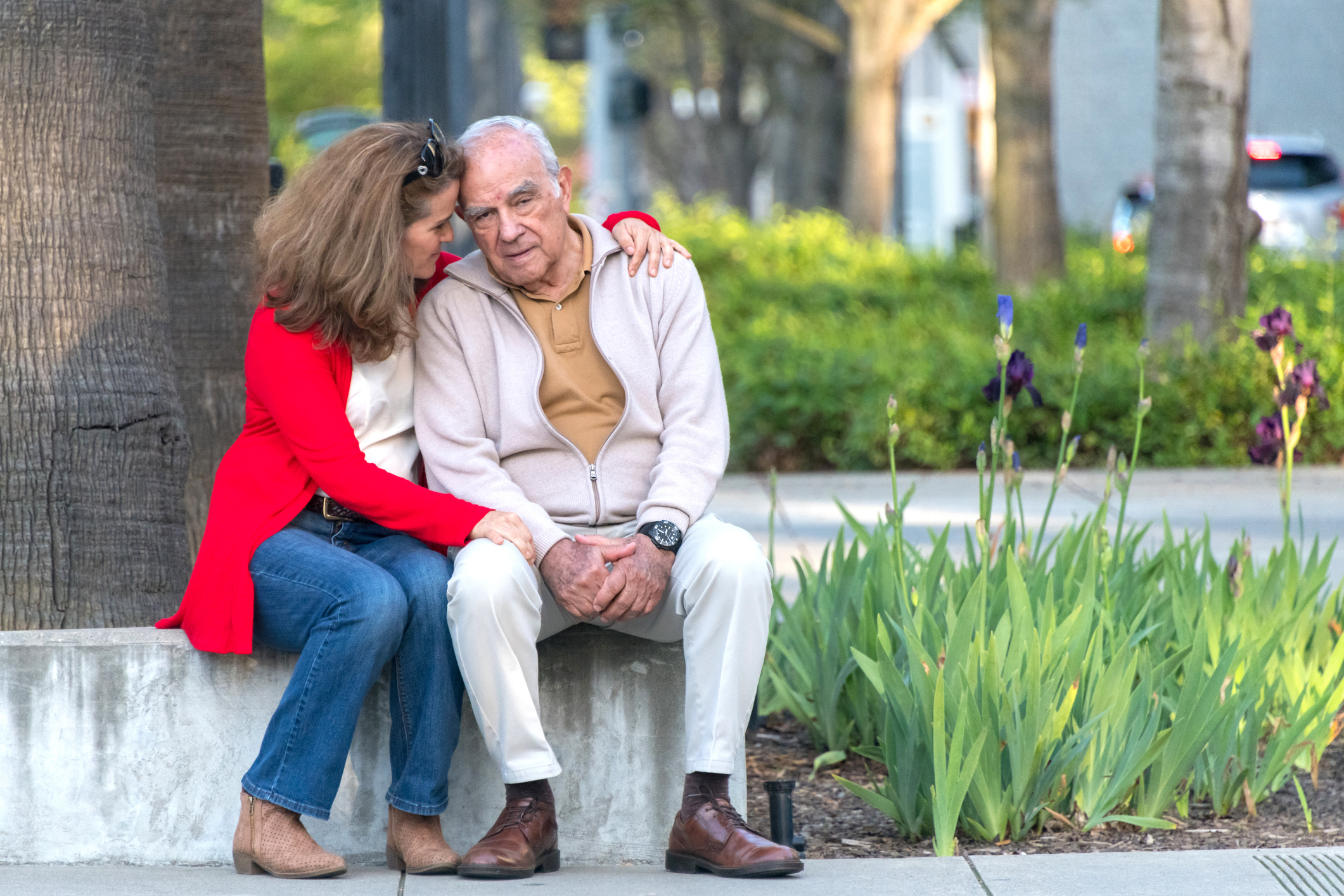 senior Hispanic or middle Eastern man posing with his mature caucasian daughter in the street, she is comforting him