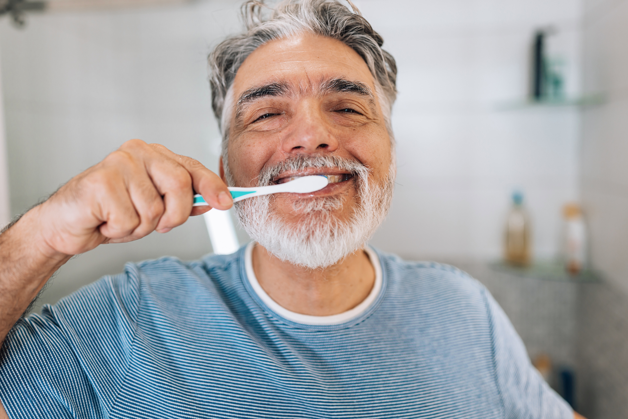 Cheerful mature man in pajamas washing teeth close up
