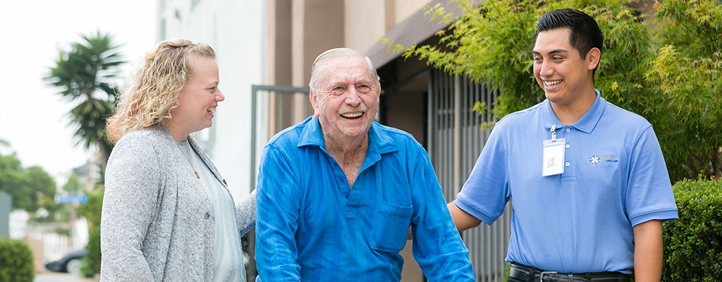 two caregivers walking with senior man outside