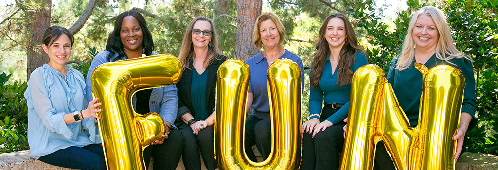 Team group photo while holding balloons that spell 'FUN'
